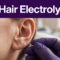 Gloved practitioner treating hair near an outer ear in a clean clinic.